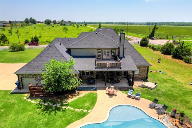 rear view of property featuring a lawn, stone siding, a patio, a shingled roof, and a balcony