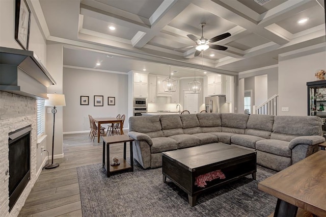 living room featuring coffered ceiling, a fireplace, wood-type flooring, and ornamental molding