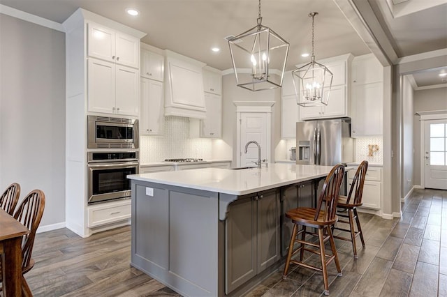 kitchen featuring pendant lighting, a breakfast bar, appliances with stainless steel finishes, a kitchen island with sink, and white cabinetry