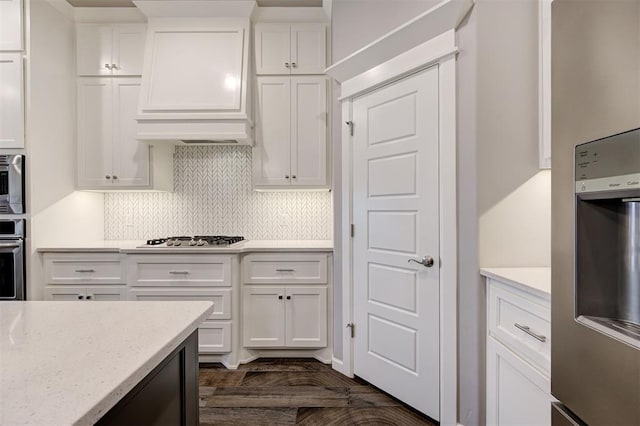 kitchen featuring light stone counters, appliances with stainless steel finishes, custom range hood, white cabinets, and backsplash