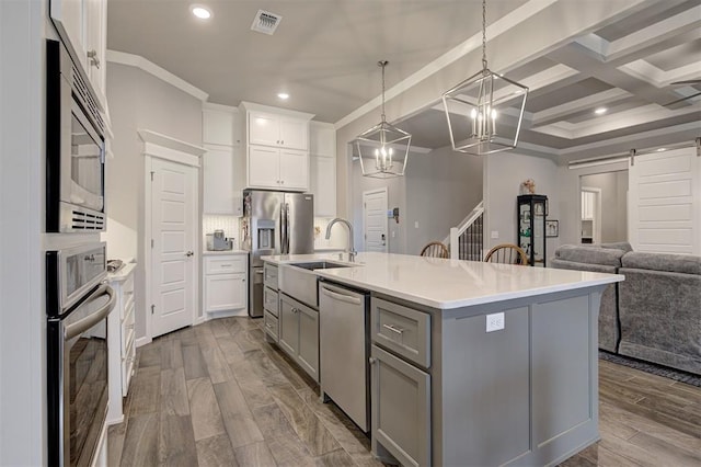 kitchen with stainless steel appliances, white cabinets, a center island with sink, decorative light fixtures, and a barn door