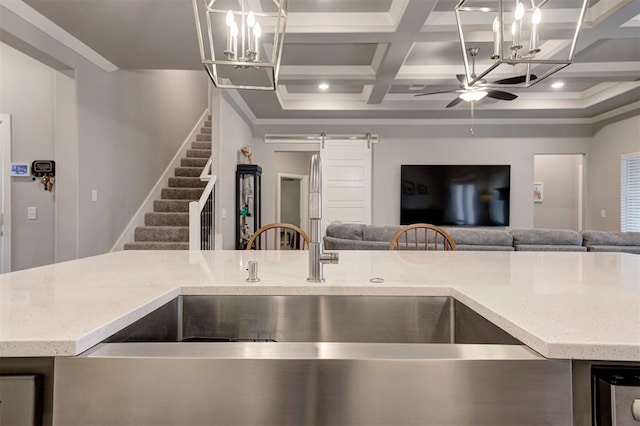 kitchen featuring ceiling fan with notable chandelier, coffered ceiling, a barn door, a center island with sink, and beam ceiling