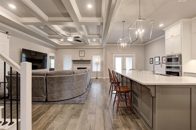 living room featuring dark hardwood / wood-style floors, ceiling fan with notable chandelier, beamed ceiling, sink, and coffered ceiling