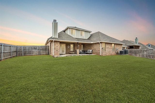 back house at dusk with a patio, central AC, and a lawn