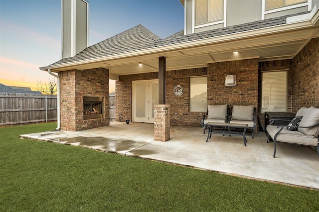 patio terrace at dusk with an outdoor brick fireplace and a lawn