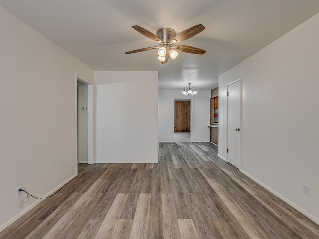 empty room with ceiling fan with notable chandelier and light hardwood / wood-style flooring