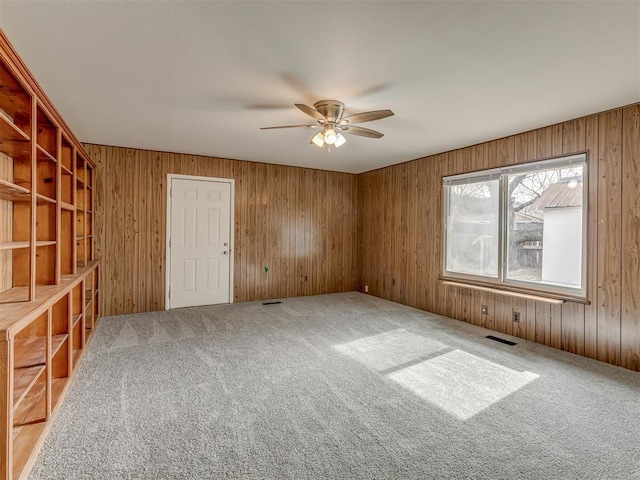 spare room with carpet flooring, wooden walls, and ceiling fan