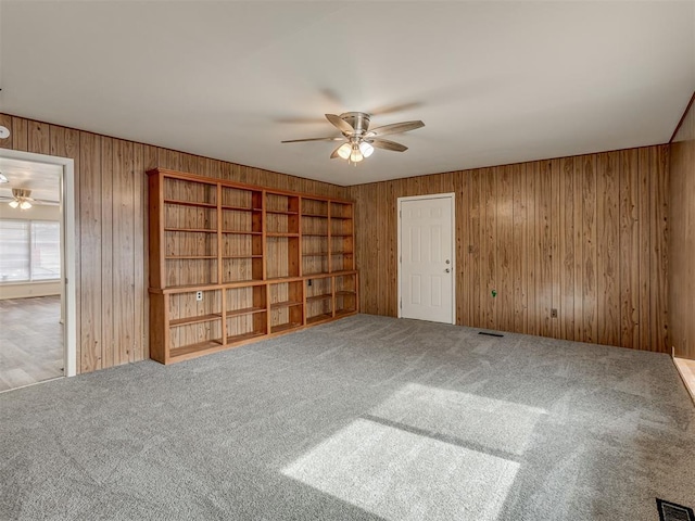 carpeted spare room featuring ceiling fan and wood walls