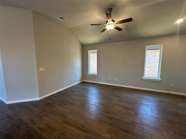 empty room featuring lofted ceiling, dark wood-style flooring, a ceiling fan, visible vents, and baseboards