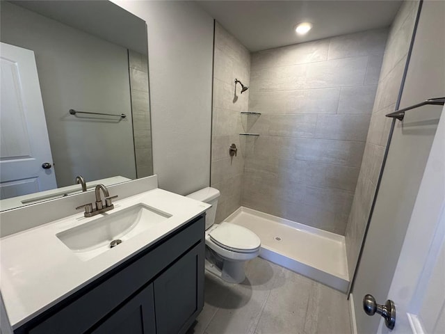 bathroom with a tile shower, vanity, and toilet