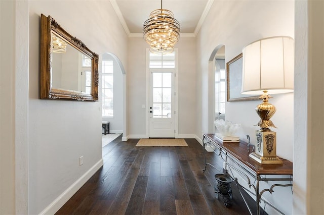 foyer entrance with dark wood-type flooring, ornamental molding, and an inviting chandelier