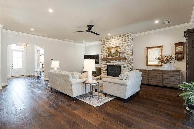 living room with ceiling fan, a stone fireplace, crown molding, and dark wood-type flooring