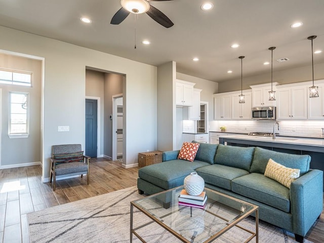 living room with ceiling fan, sink, and light wood-type flooring