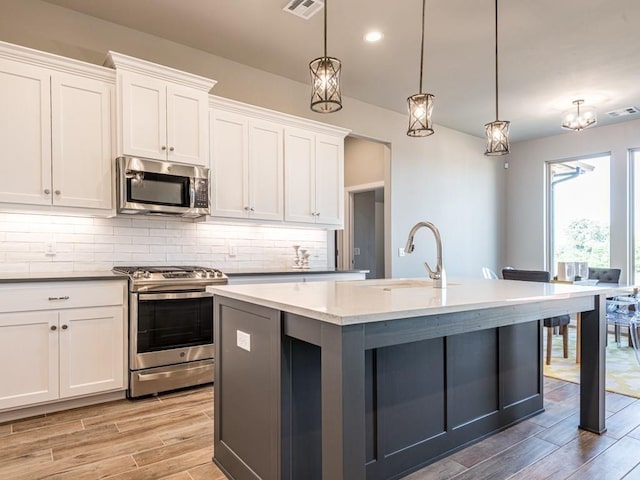 kitchen featuring white cabinets, pendant lighting, appliances with stainless steel finishes, and a kitchen island with sink