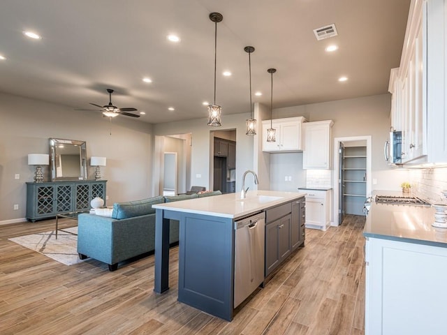 kitchen with hanging light fixtures, appliances with stainless steel finishes, backsplash, white cabinetry, and a center island with sink