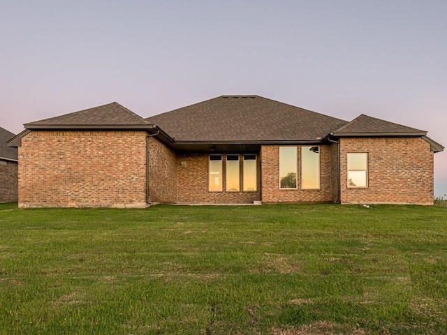 back house at dusk featuring a lawn