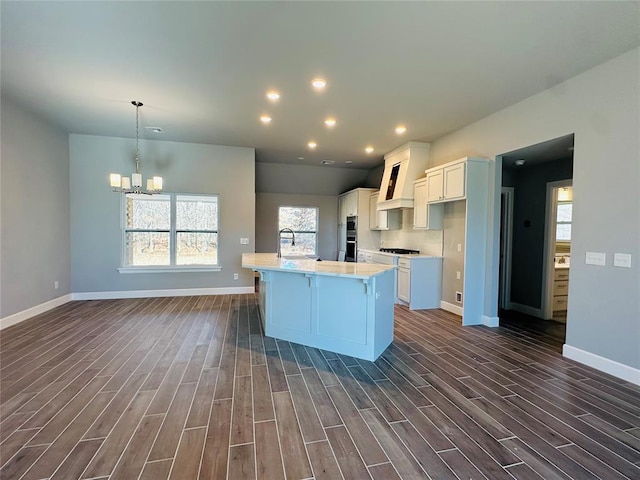 kitchen with pendant lighting, dark hardwood / wood-style flooring, sink, a kitchen island with sink, and a chandelier