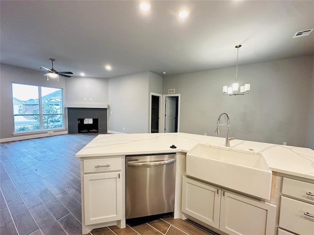 kitchen with a fireplace, stainless steel dishwasher, sink, light stone countertops, and ceiling fan with notable chandelier