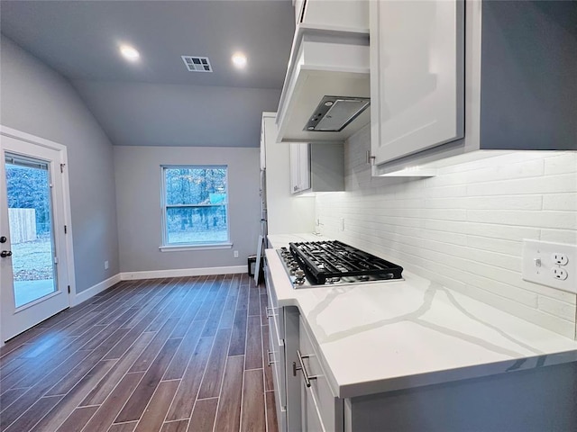 kitchen with lofted ceiling, custom exhaust hood, stainless steel gas cooktop, light stone countertops, and dark hardwood / wood-style flooring