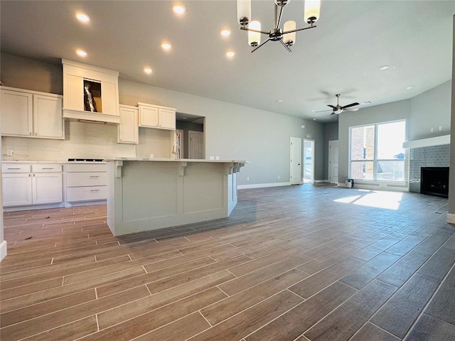 kitchen with ceiling fan with notable chandelier, a center island, white cabinetry, a fireplace, and light wood-type flooring