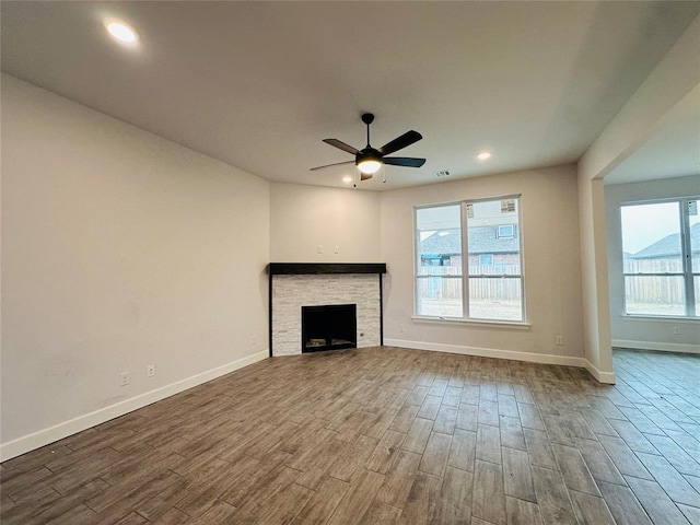 unfurnished living room featuring ceiling fan, baseboards, a stone fireplace, recessed lighting, and wood finished floors