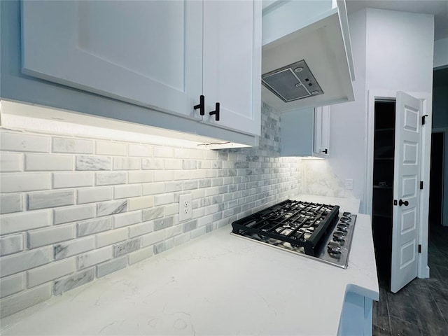 kitchen with tasteful backsplash, light stone countertops, under cabinet range hood, stainless steel gas stovetop, and white cabinetry