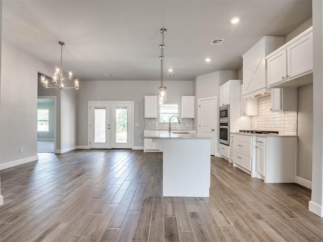 kitchen featuring light hardwood / wood-style floors, a center island with sink, stainless steel appliances, pendant lighting, and white cabinets