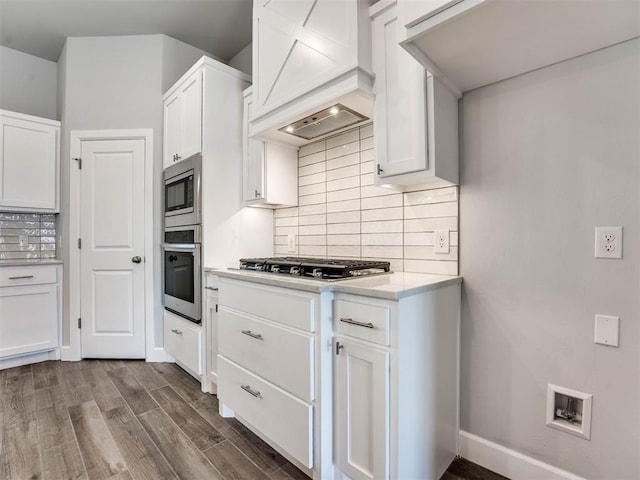 kitchen featuring appliances with stainless steel finishes, white cabinetry, dark hardwood / wood-style flooring, decorative backsplash, and premium range hood