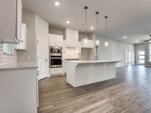 kitchen featuring custom exhaust hood, white cabinetry, stainless steel appliances, ceiling fan, and a center island with sink