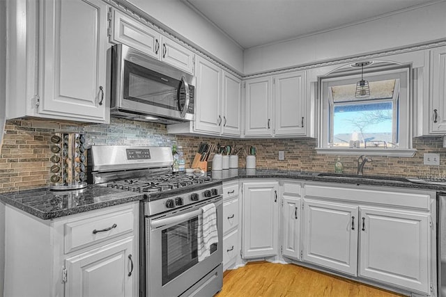 kitchen with white cabinetry, stainless steel appliances, dark stone countertops, decorative backsplash, and sink