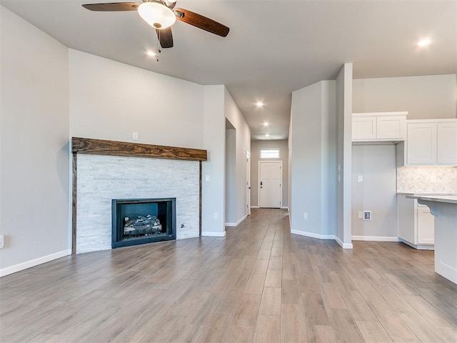 unfurnished living room featuring light wood-type flooring, ceiling fan, and a stone fireplace