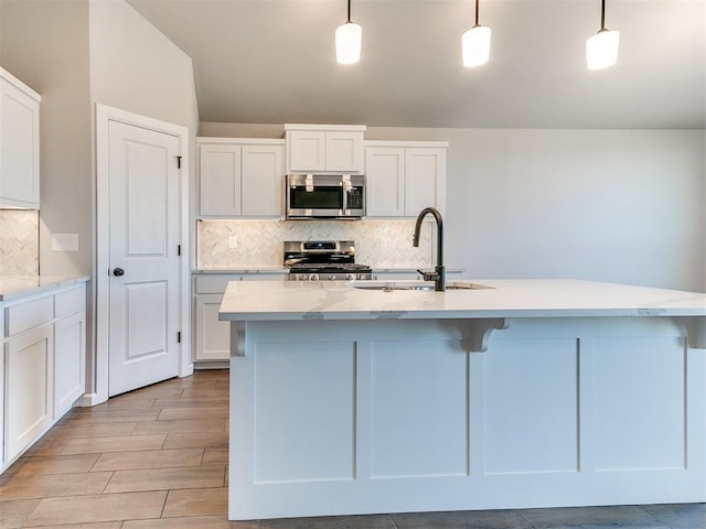 kitchen with appliances with stainless steel finishes, an island with sink, and pendant lighting