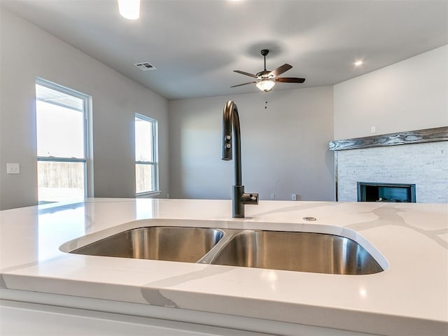 kitchen with ceiling fan, light stone counters, sink, and a stone fireplace