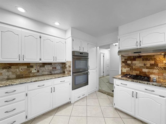 kitchen with light tile patterned flooring, tasteful backsplash, dark stone countertops, double oven, and white cabinets