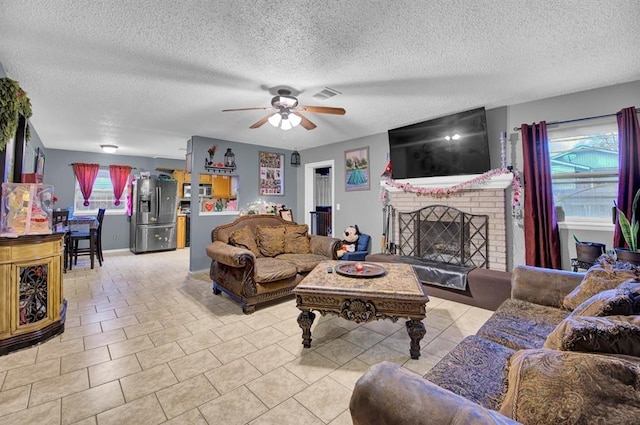 tiled living room featuring a textured ceiling, a brick fireplace, and ceiling fan