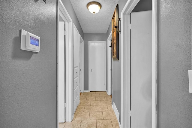 hall with a textured ceiling and light tile patterned floors