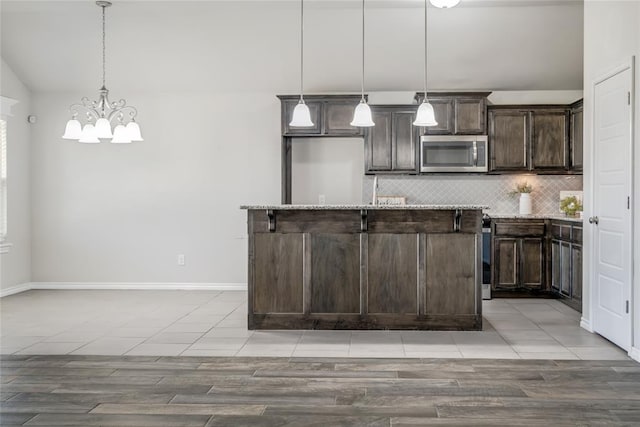 kitchen featuring vaulted ceiling, decorative light fixtures, backsplash, a kitchen island with sink, and dark brown cabinetry