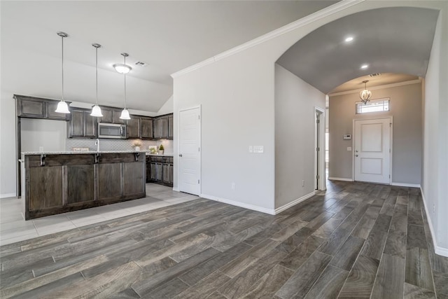 kitchen featuring pendant lighting, lofted ceiling, dark brown cabinetry, wood-type flooring, and a center island with sink