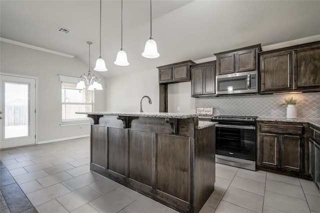 kitchen with appliances with stainless steel finishes, hanging light fixtures, a kitchen island with sink, and a breakfast bar area