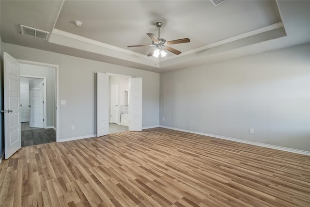 unfurnished bedroom featuring ceiling fan, connected bathroom, a raised ceiling, and light hardwood / wood-style flooring