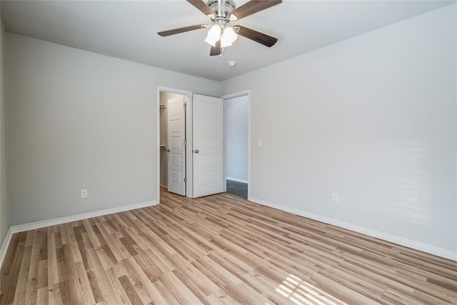 unfurnished bedroom with a spacious closet, a closet, ceiling fan, and light wood-type flooring