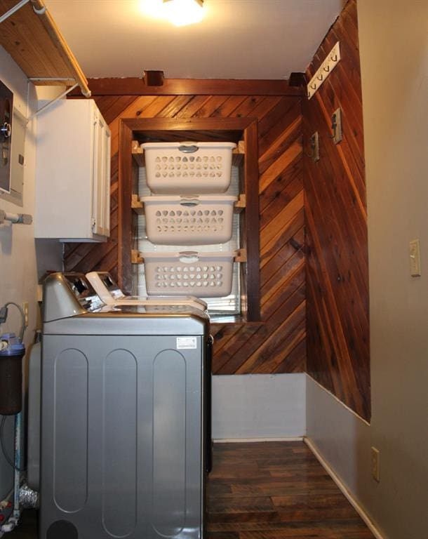 clothes washing area with cabinets, washer and clothes dryer, dark hardwood / wood-style floors, and wood walls