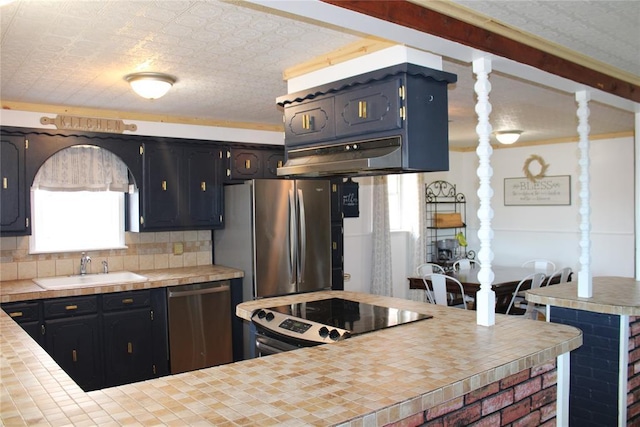 kitchen with a textured ceiling, stainless steel appliances, sink, backsplash, and tile countertops