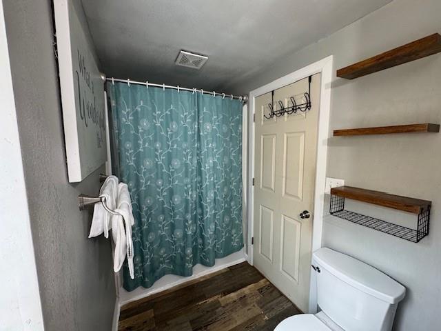 bathroom with curtained shower, wood-type flooring, and toilet