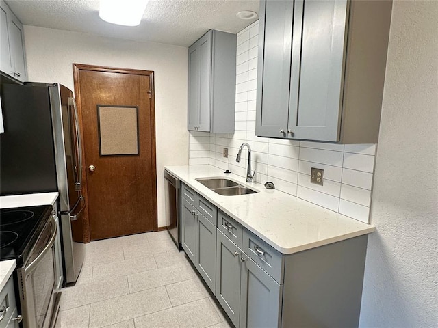 kitchen featuring backsplash, gray cabinets, sink, stainless steel appliances, and a textured ceiling