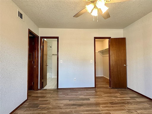 unfurnished bedroom featuring hardwood / wood-style floors, a textured ceiling, a walk in closet, a closet, and ceiling fan