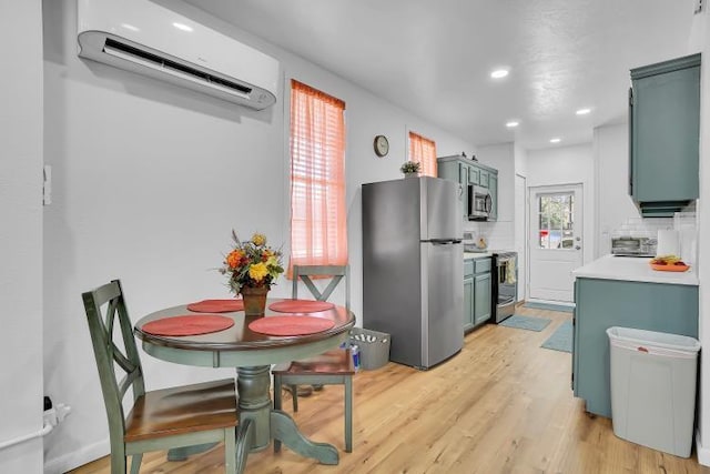 kitchen with appliances with stainless steel finishes, tasteful backsplash, a wall unit AC, light hardwood / wood-style flooring, and blue cabinets