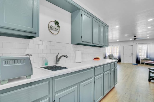 kitchen featuring ceiling fan, sink, backsplash, and light wood-type flooring