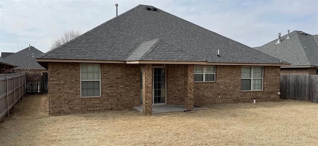 back of house featuring a yard, a fenced backyard, brick siding, and roof with shingles