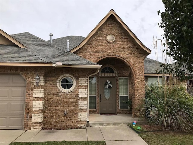 entrance to property featuring a shingled roof, brick siding, and an attached garage